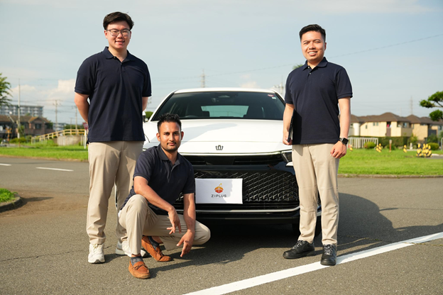 Học bằng lái xe tại Nhật Bản với Ziplus Ba người đàn ông đứng cạnh xe ô tô màu trắng mang logo Ziplus